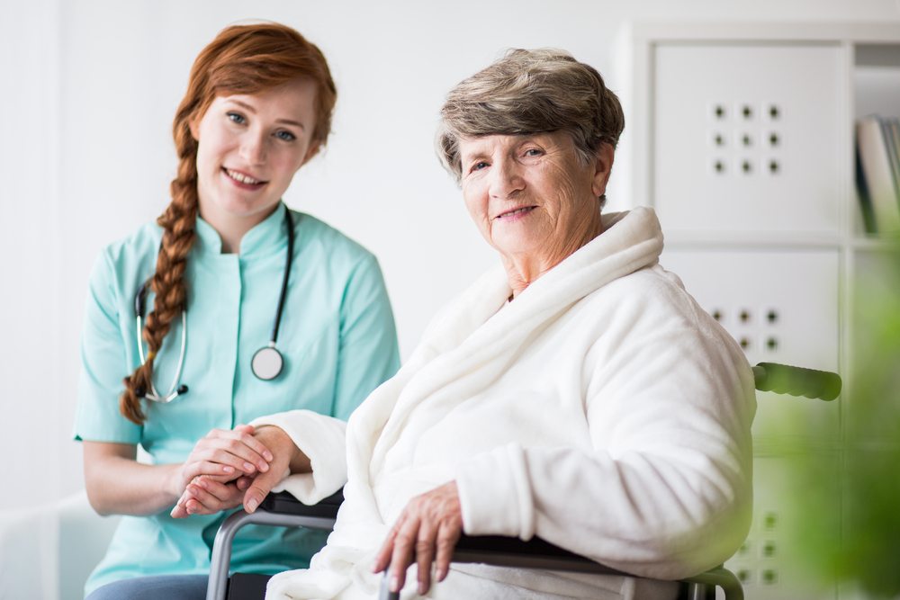 Nurse holding hand of elderly woman in wheelchair