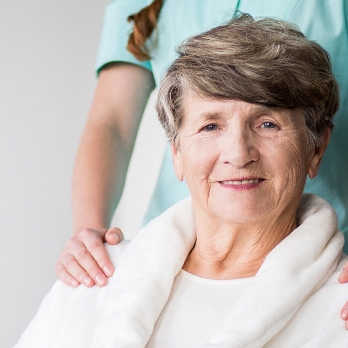 Smiling elderly woman with caregiver's hands on shoulders