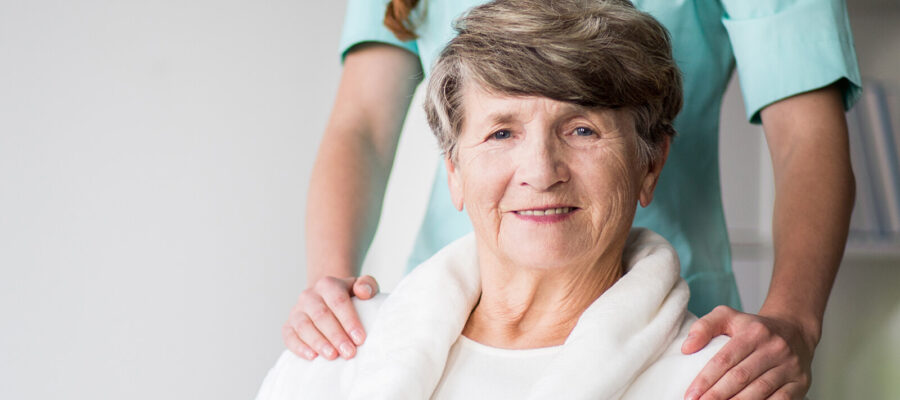 Smiling elderly woman with caregiver's hands on shoulders