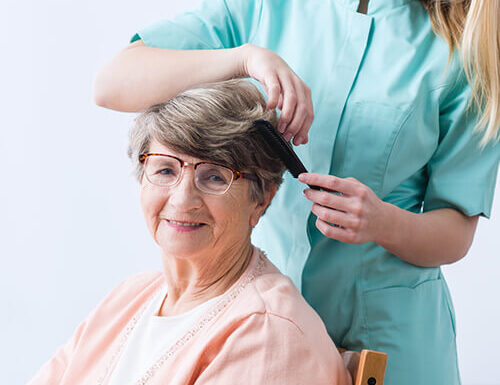 Caregiver brushing elderly woman's hair, both smiling