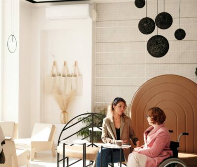 Two women conversing indoors, one in wheelchair